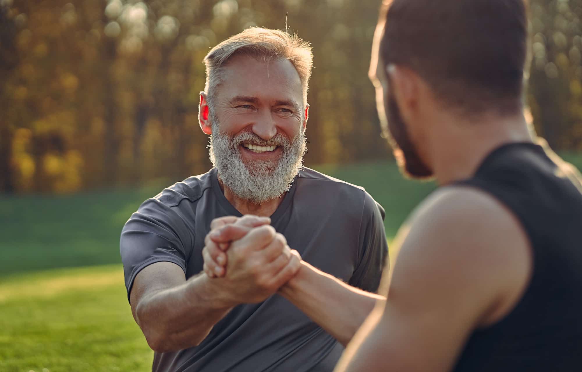 Two men arm wrestling outdoors.
