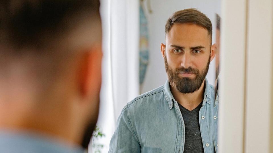 a man checks himself in a mirror for signs of an alcoholic face.