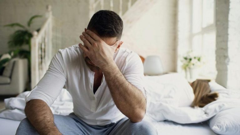 Lorazepam vs Xanax hero image of a man with his hand over his face while sitting in bed.